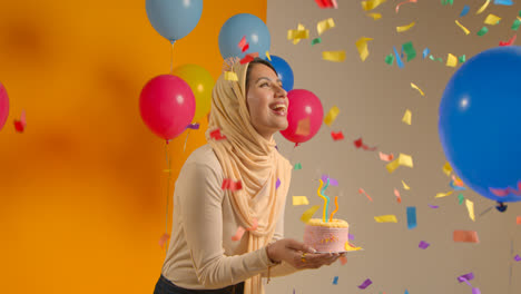 Studioporträt-Einer-Frau-Mit-Hijab-Und-Geburtstagsstirnband,-Die-Ihren-Geburtstag-Feiert-Und-Kerzen-Auf-Dem-Kuchen-Ausbläst